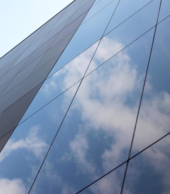 A low angle shot of a glass high-rise business building with a reflection of clouds and the sky on it